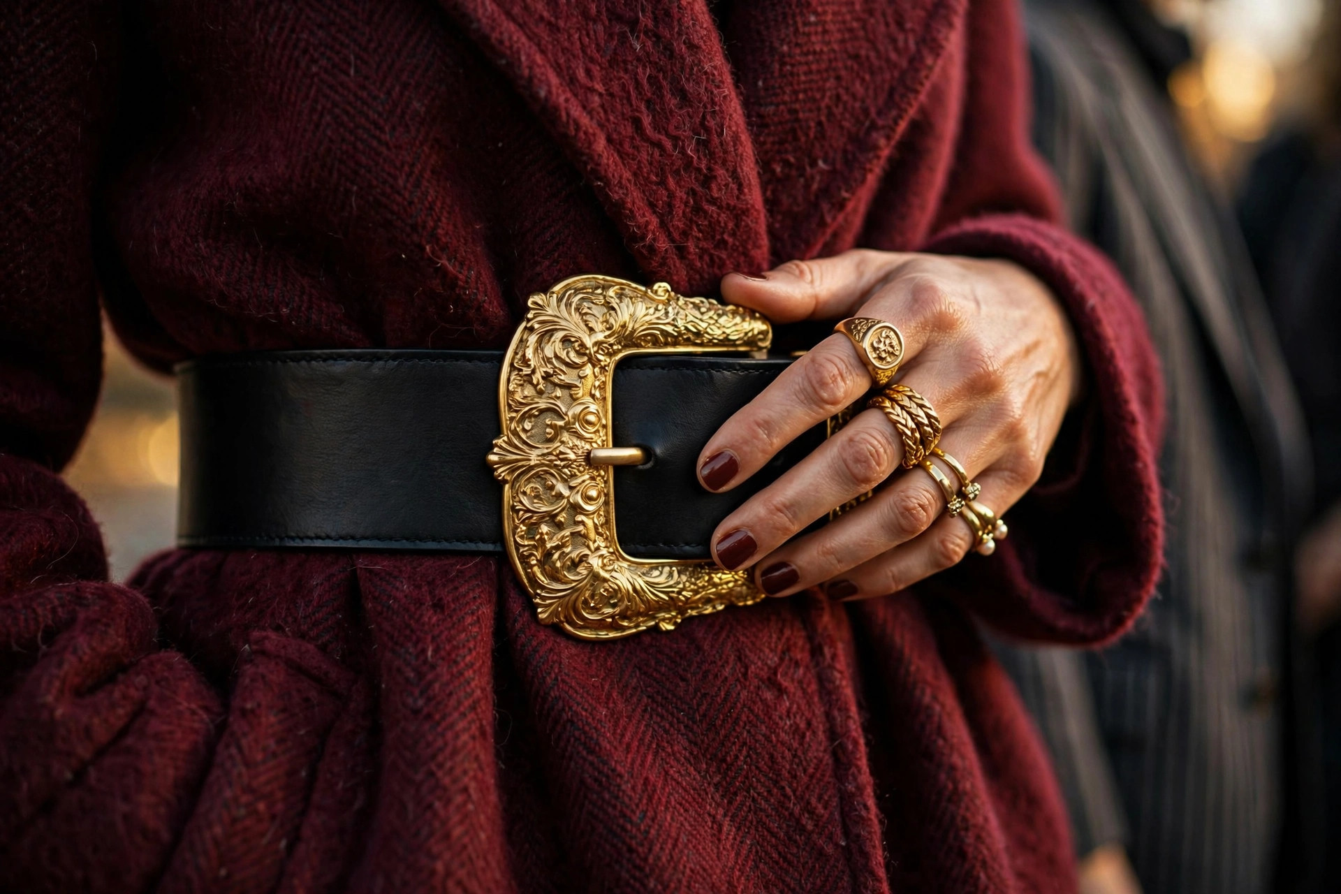 Close-up of wide black statement belt with oversized ornate gold buckle on a burgundy wool coat