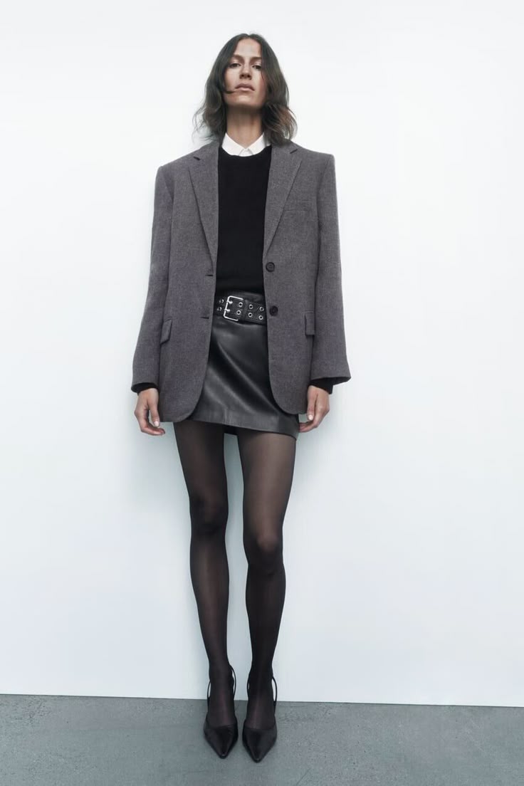 Woman wearing a gray oversized blazer with a black leather mini skirt, sheer tights and boots