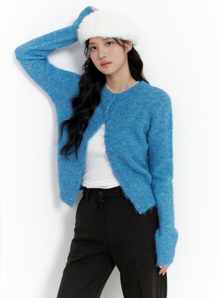 Woman in a frosted blue fuzzy cardigan with a white beanie and black trousers