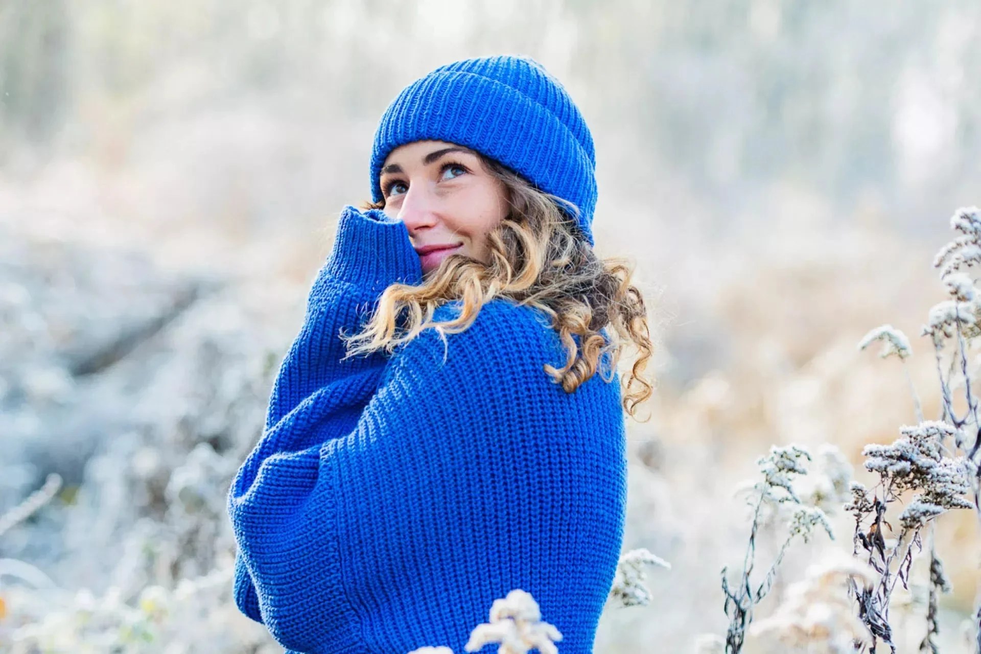 Woman in a bright blue chunky knit sweater and matching beanie in the snow