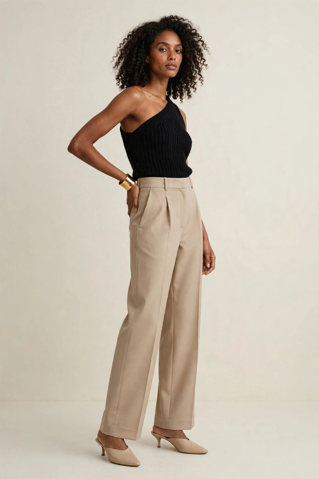 Woman in a black one-shoulder knit top with high-waist trousers, asymmetric neckline runway trend outfit