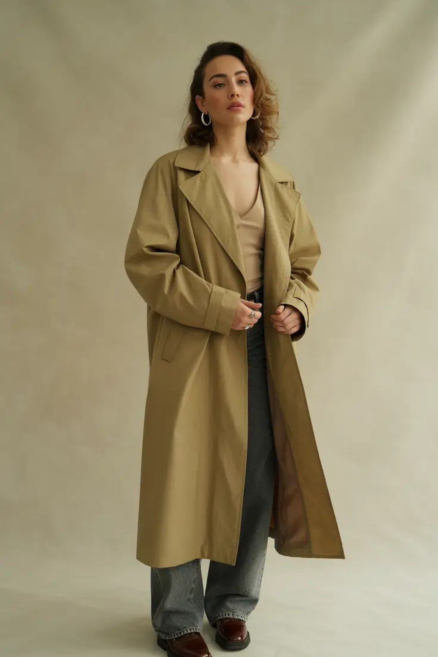 Oversized beige trench coat worn open over a neutral top and jeans